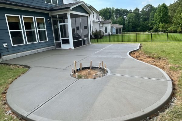 Newly poured curved concrete patio with circular fire pit space in a backyard by Limitless Boundaries LLC, Raleigh NC
